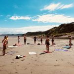 Yoga på stranden før surfing i New Zealand