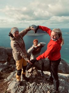 To elever fra Vefsn Folkehøgskole Toppen i front, som lager et hjerte med hendene. Inne i hjertet kan man se en elev som står bak. I bakgrunnen hav og fjell.