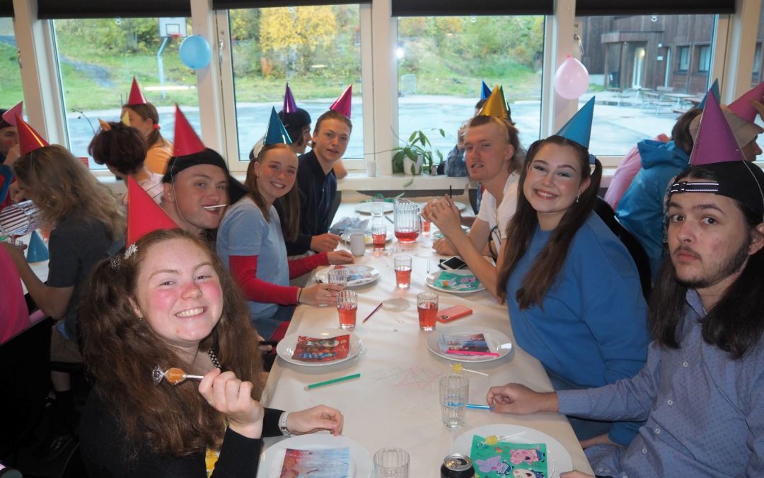 Elever sitter kledd som barn og med partyhatter rundt middagsbord.