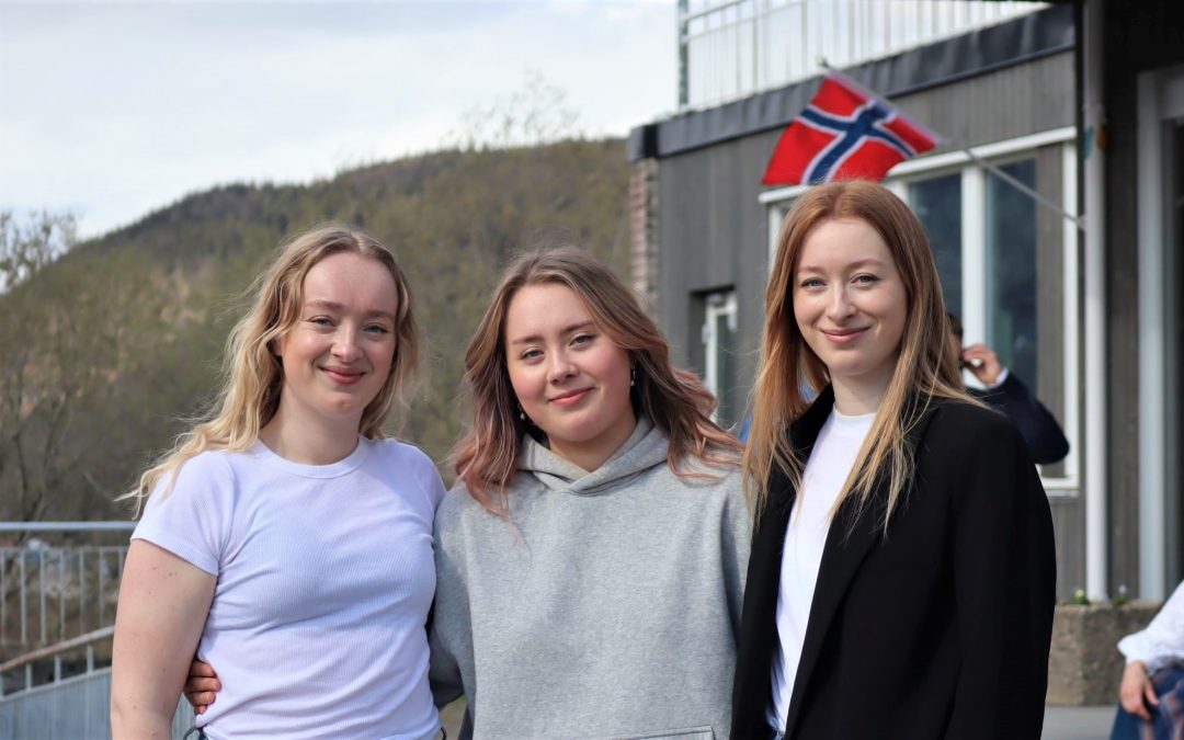 Josefine, Johanne og Jonette Taraldsen foran hovedinngangen på Vefsn Folkehøgskole Toppen. Skoleavslutningen 2023. Det norske flagg i bakgrunnen.