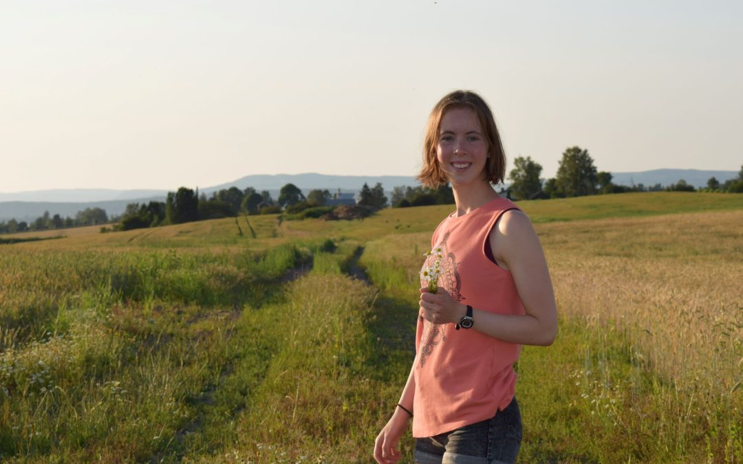 Kathrine Sollien, tidligere elev på Vefsn Folkehøgskole Toppen står med en bukett markblomster ute på en eng.
