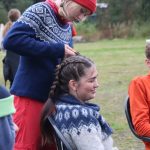 Elev fra Vefsn Folkehøgskole Toppen med rød lue står og fletter håret til en annen elev. Ute rundt et bål, begge med ullgensere.