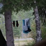 En jakke og et par sokker henger til tørk på ei snor som er bundet mellom to trær.