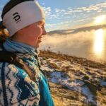 Elev fra Vefsn Folkehøgskole Toppen i profil, ser ut over landskapet. Strikket genser og lue. I bakgrunnen solnedgang og frostrøyk over fjorden.