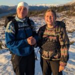 To elever fra Vefsn Folkehøgskole Toppen på tur. Holder hender og smiler mot kamera. Vinter og sol.