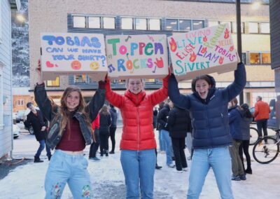 Tre elever fra Vefsn Folkehøgskole Toppen utenfor Bakgården Kultur i Mosjøen. De holder opp plakater med Toppen Rocks etter en konsert.
